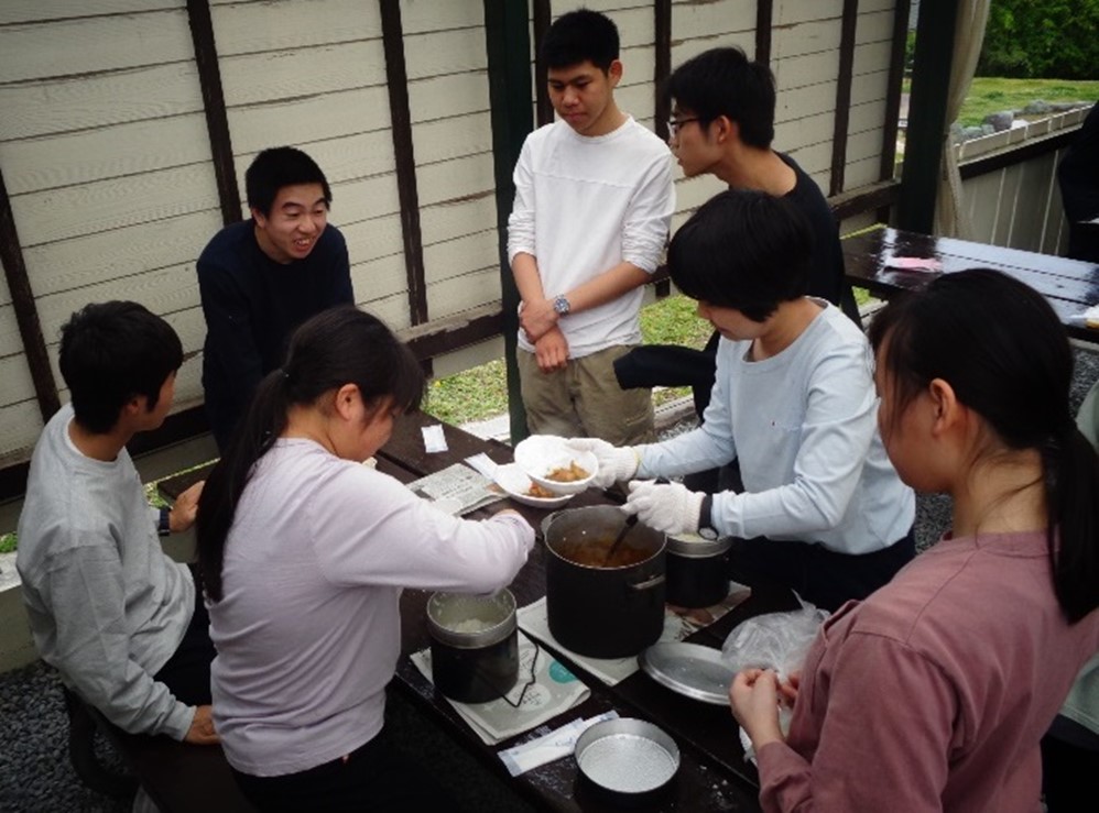 カレーが完成して鍋を囲んでみんなで盛り付けています